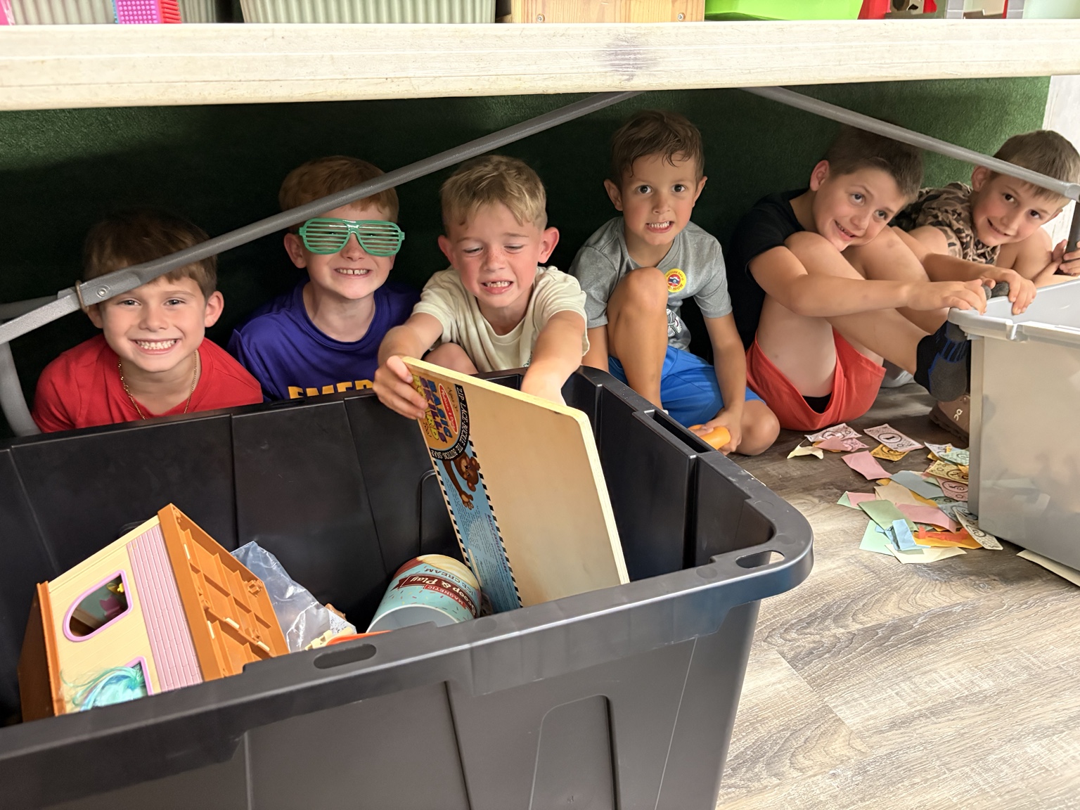 Children smiling together in a playful hideaway beneath a table