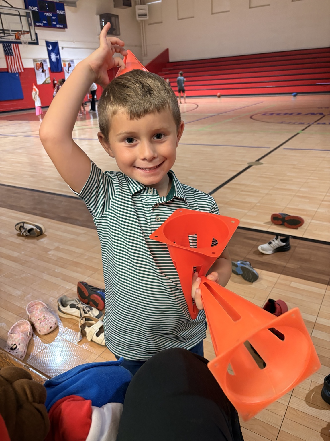 A smiling child holding orange activity cones in the gym