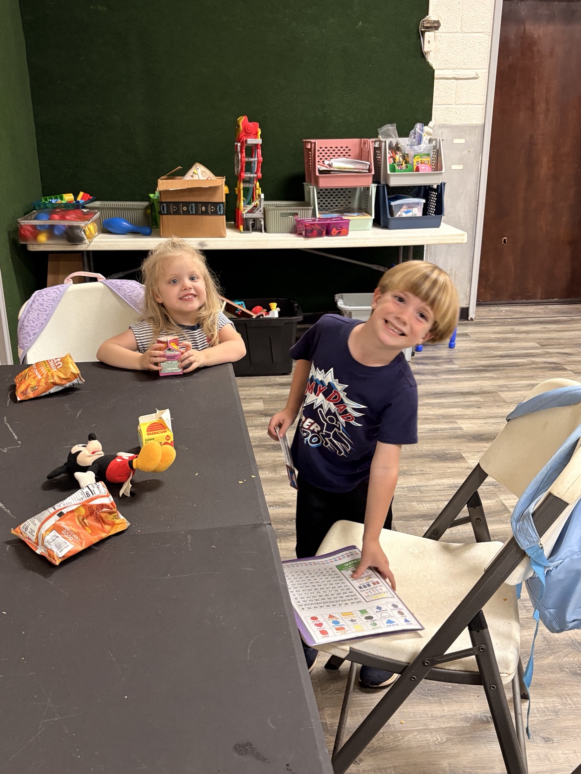 Two children smiling beside a table with snacks and activity supplies