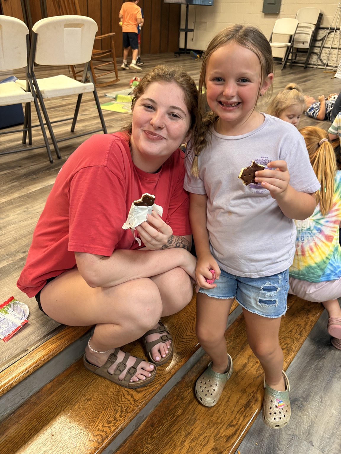 A child and an adult smiling together while enjoying ice cream sandwiches
