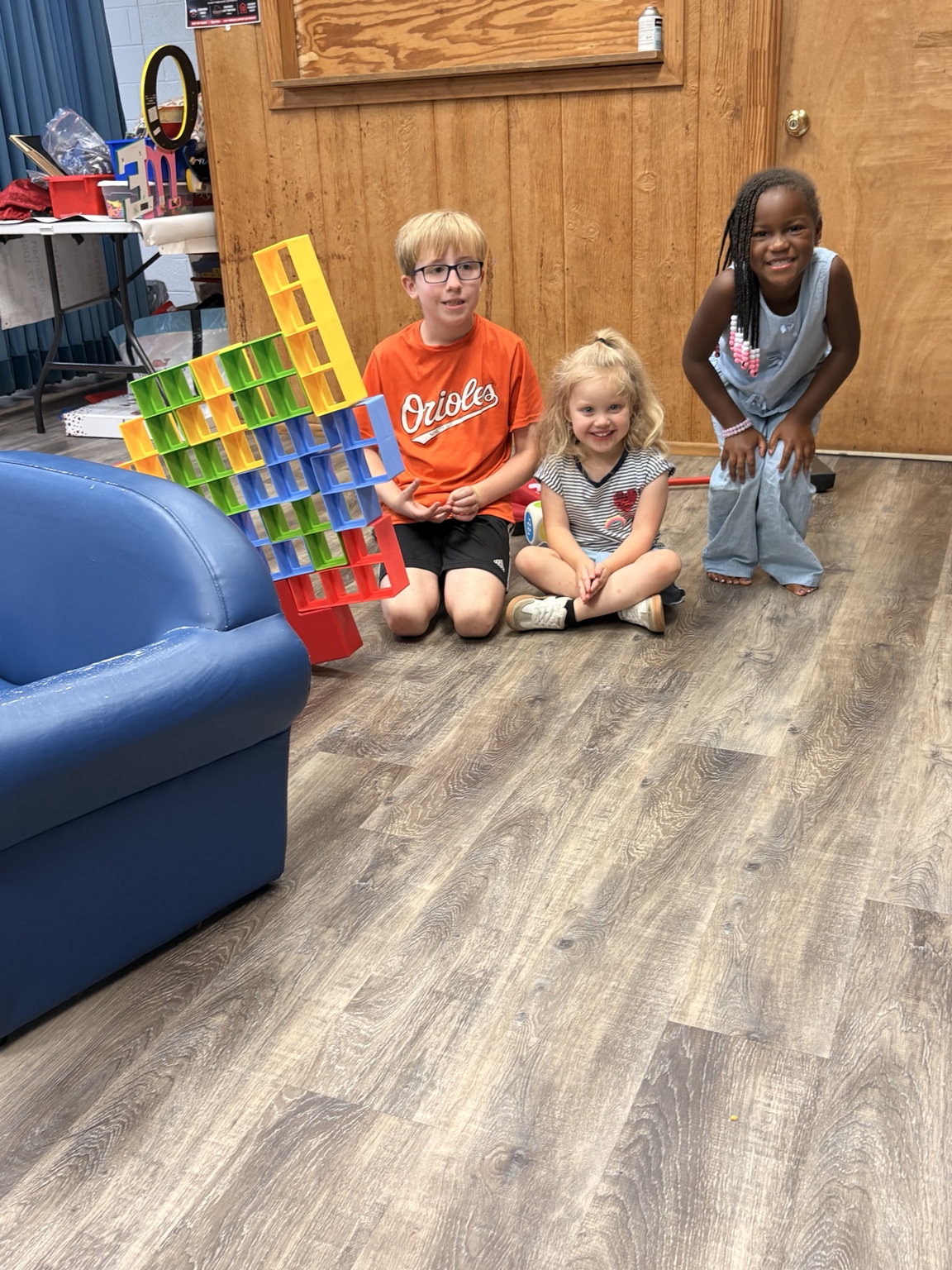 Three children showing a tall structure made from colorful building tiles