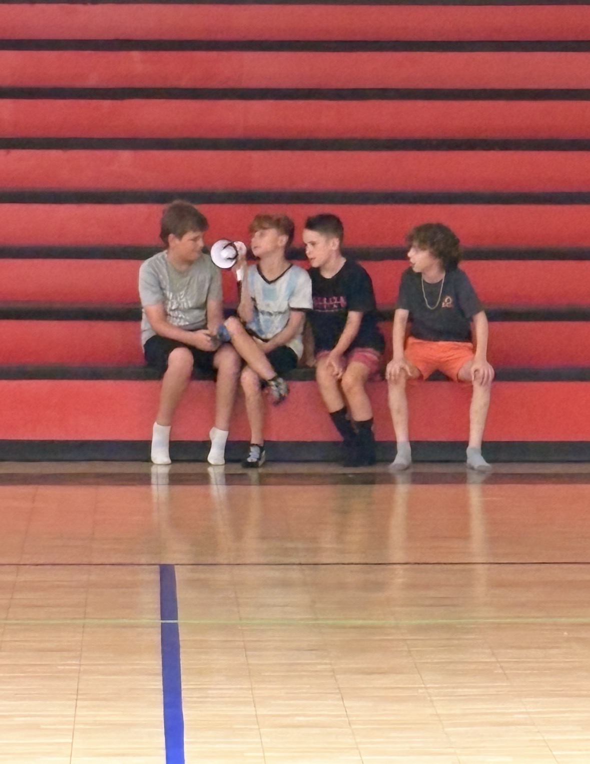 Four children sitting and talking on the gym bleachers